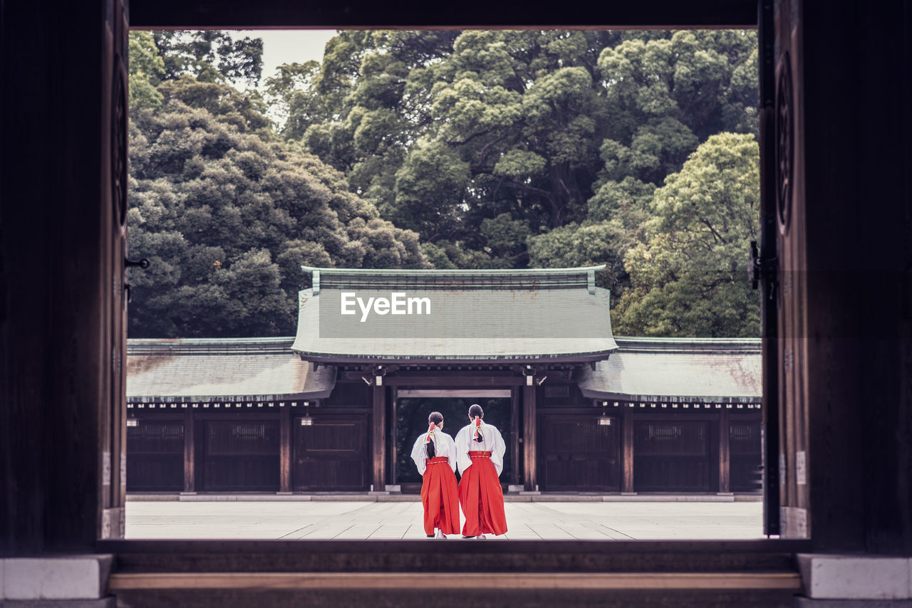 Back view of unrecognizable people in traditional kimono standing outside of ancient meiji shrine temple located in mountains in shibuya in tokyo, japan