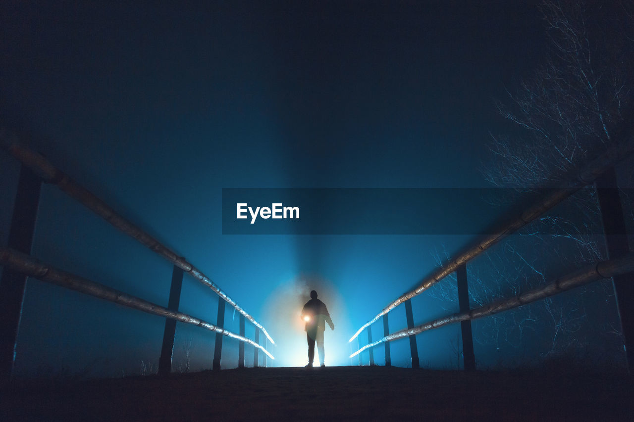 Person standing on illuminated pathway against sky at night