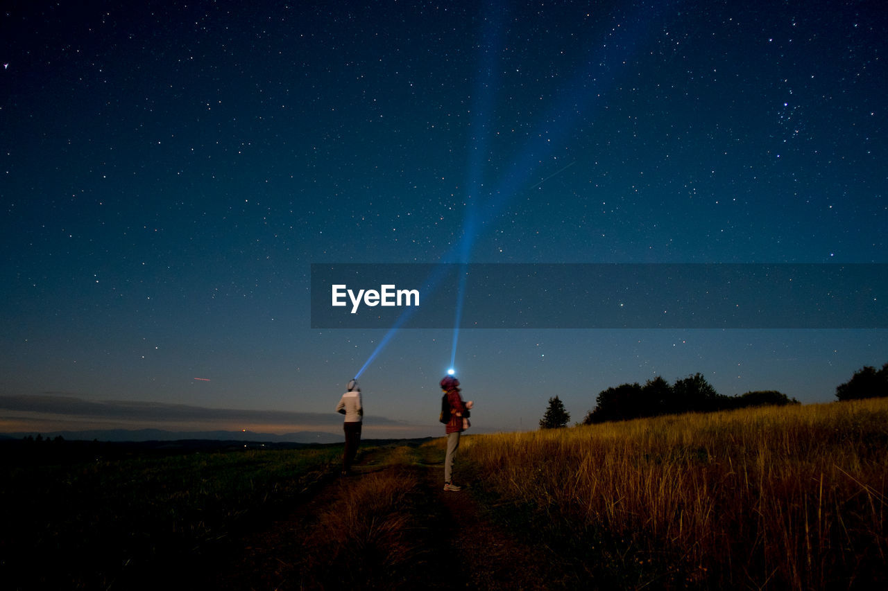People with illuminated headlamps while standing on field against starry sky at night