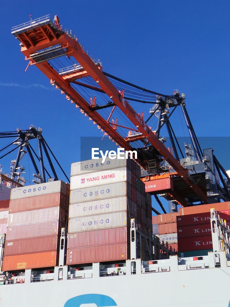 Low angle view of crane at commercial dock against blue sky