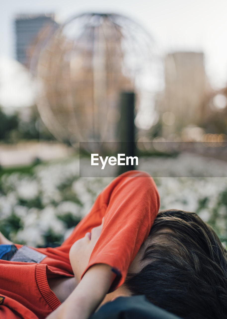 Side view of young boy lying in a city street park ground hiding face under arm covering eyes