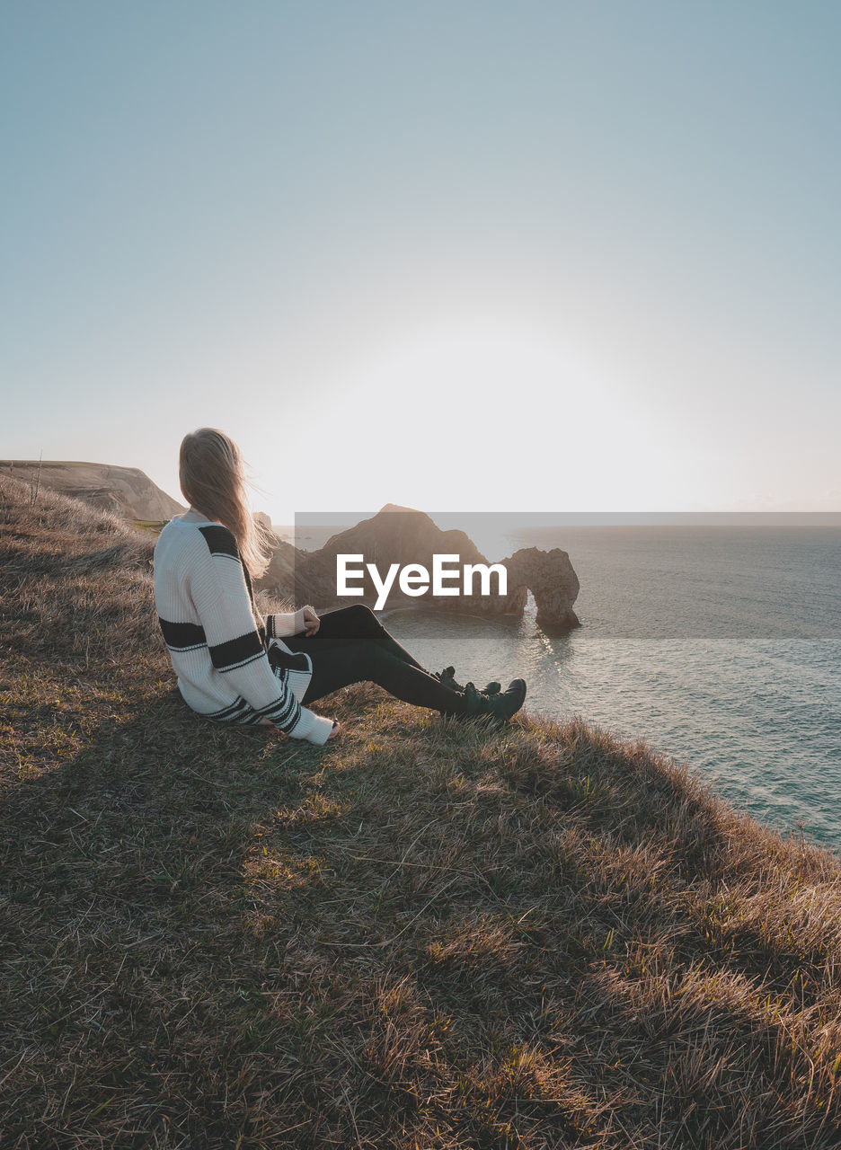 Side view of woman sitting on cliff against sea