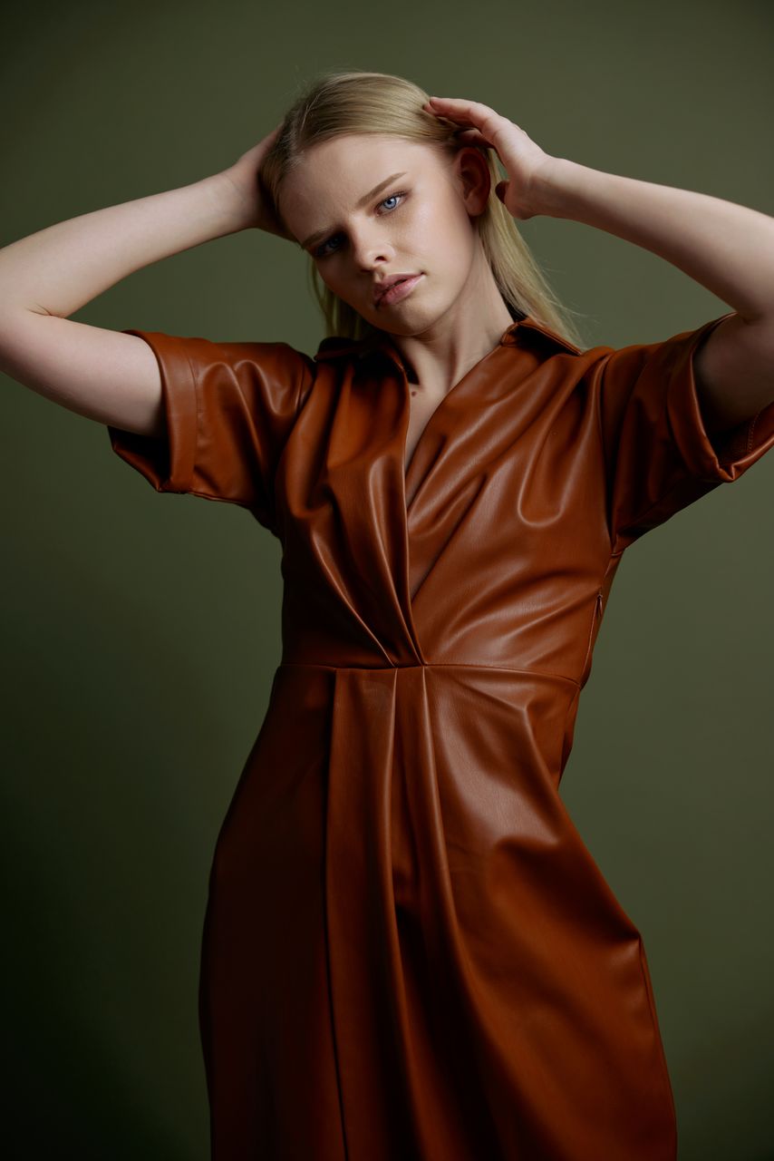 portrait of smiling young woman with arms crossed standing against wall