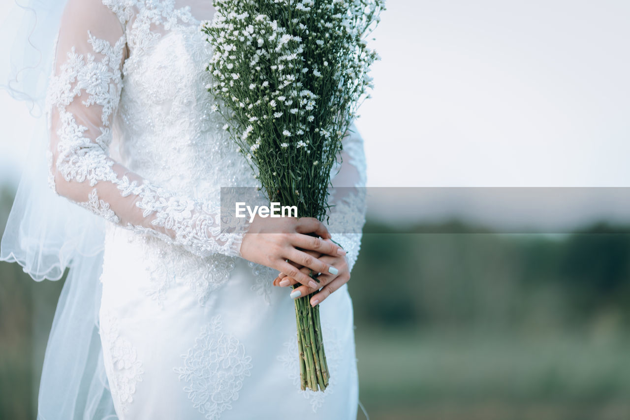 Midsection of bride holding bouquet while standing outdoors