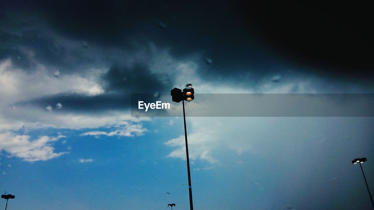 LOW ANGLE VIEW OF STREET LIGHTS AGAINST CLOUDY SKY