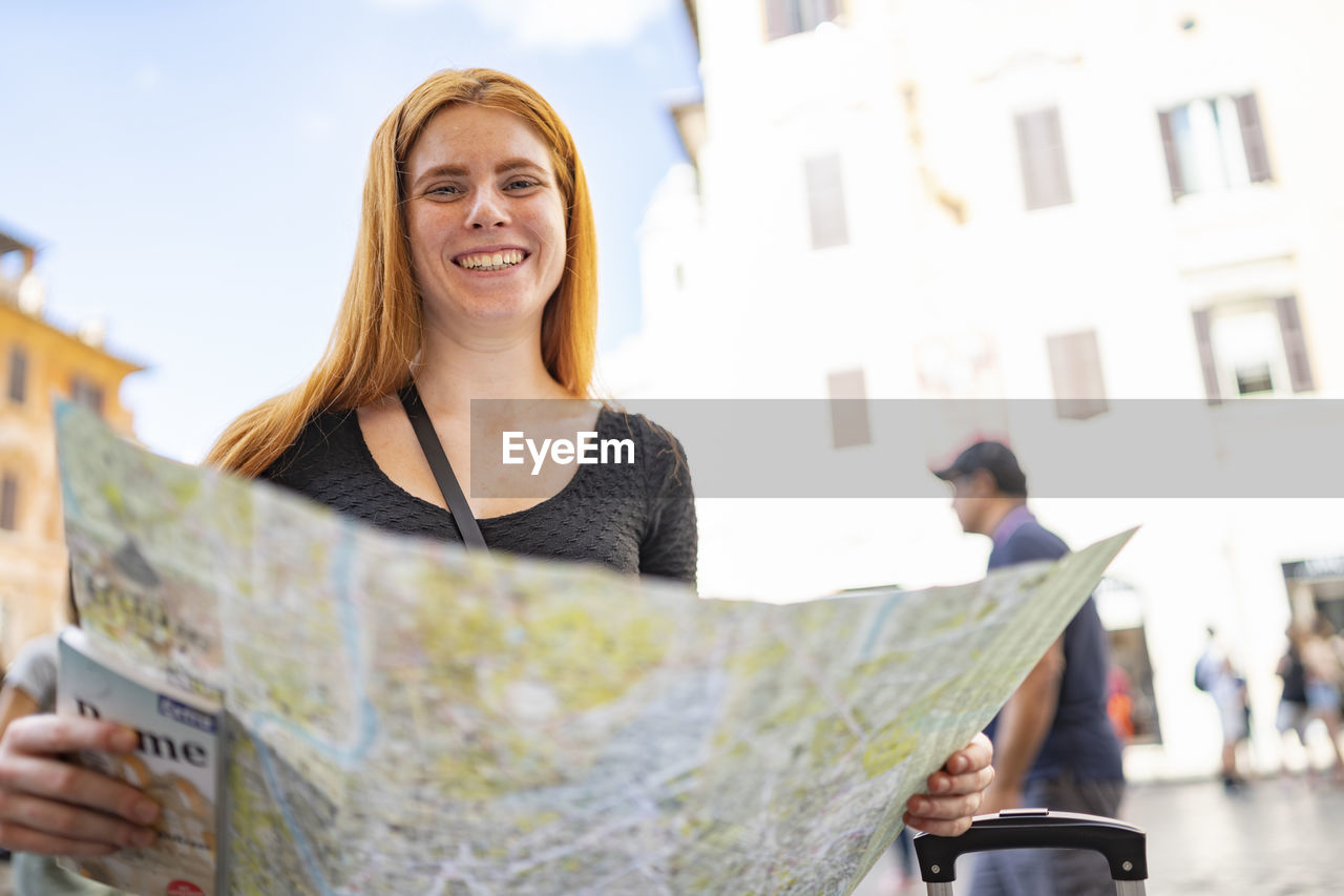 Smiling young woman with a city map is smiling looking at the camera