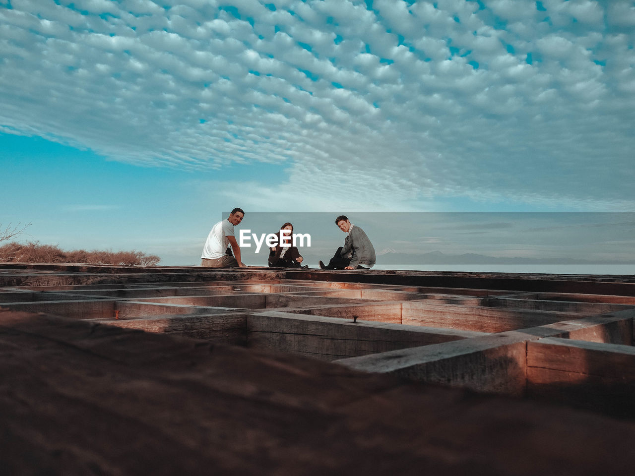 Friends sitting on wooden built structure against blue sky