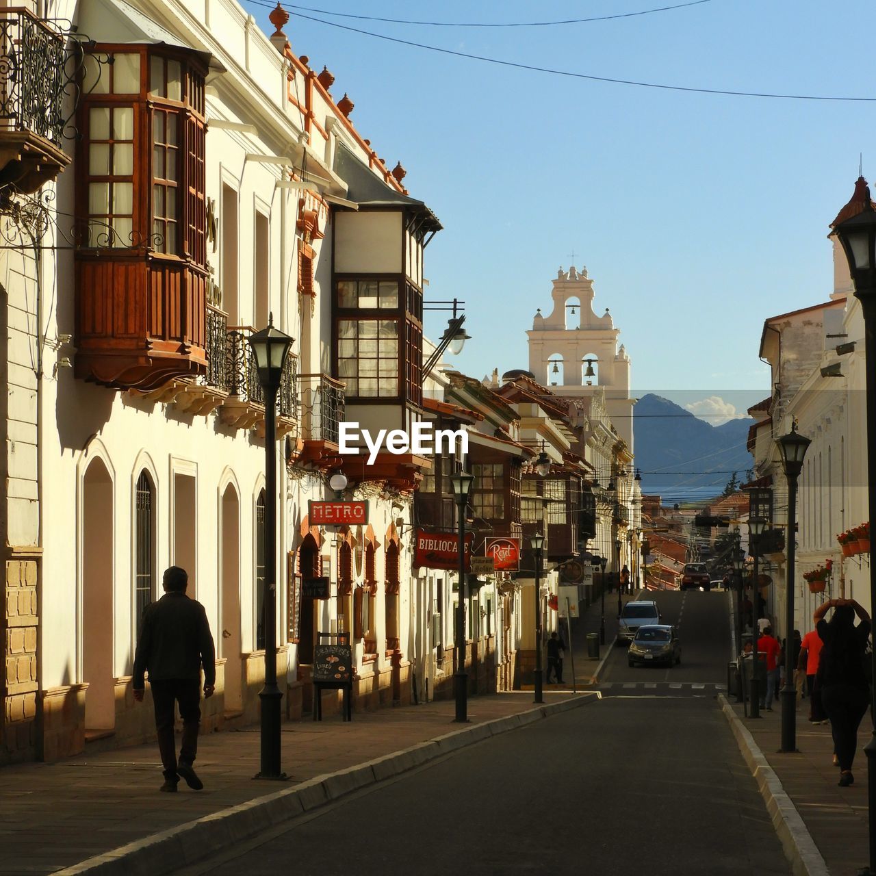 REAR VIEW OF PEOPLE WALKING ON ROAD BY BUILDINGS