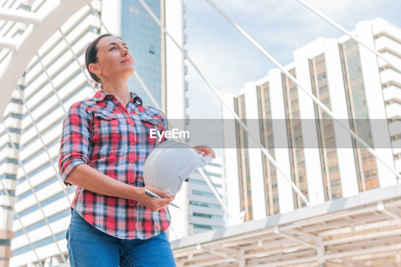 Female engineer holding hardhat while standing in city