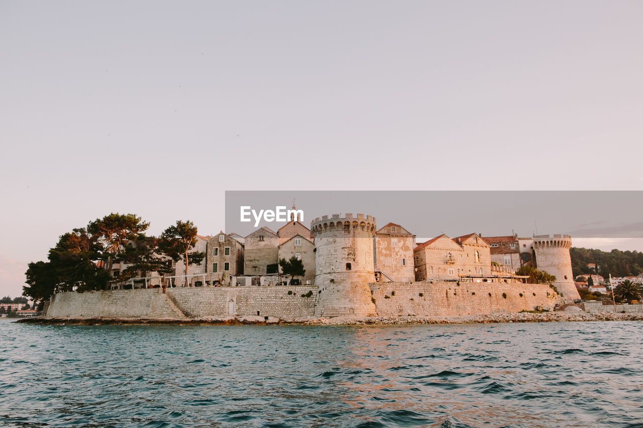 Castle by sea against clear sky at sunset