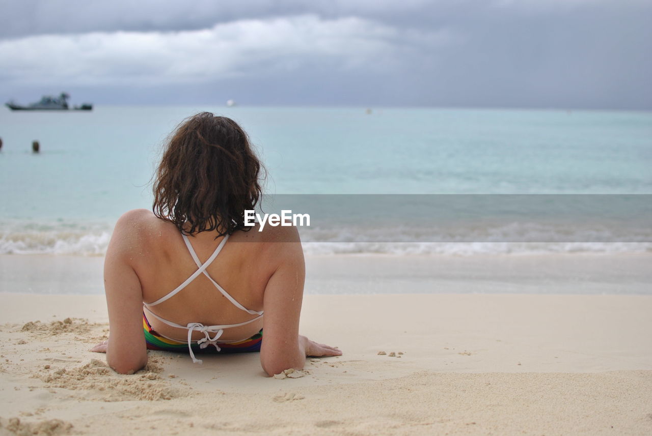 Rear view of woman relaxing at beach against sky