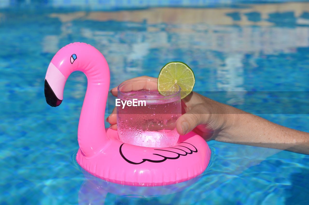 Woman in swimming pool holding glass of water on a pink flamingo float 