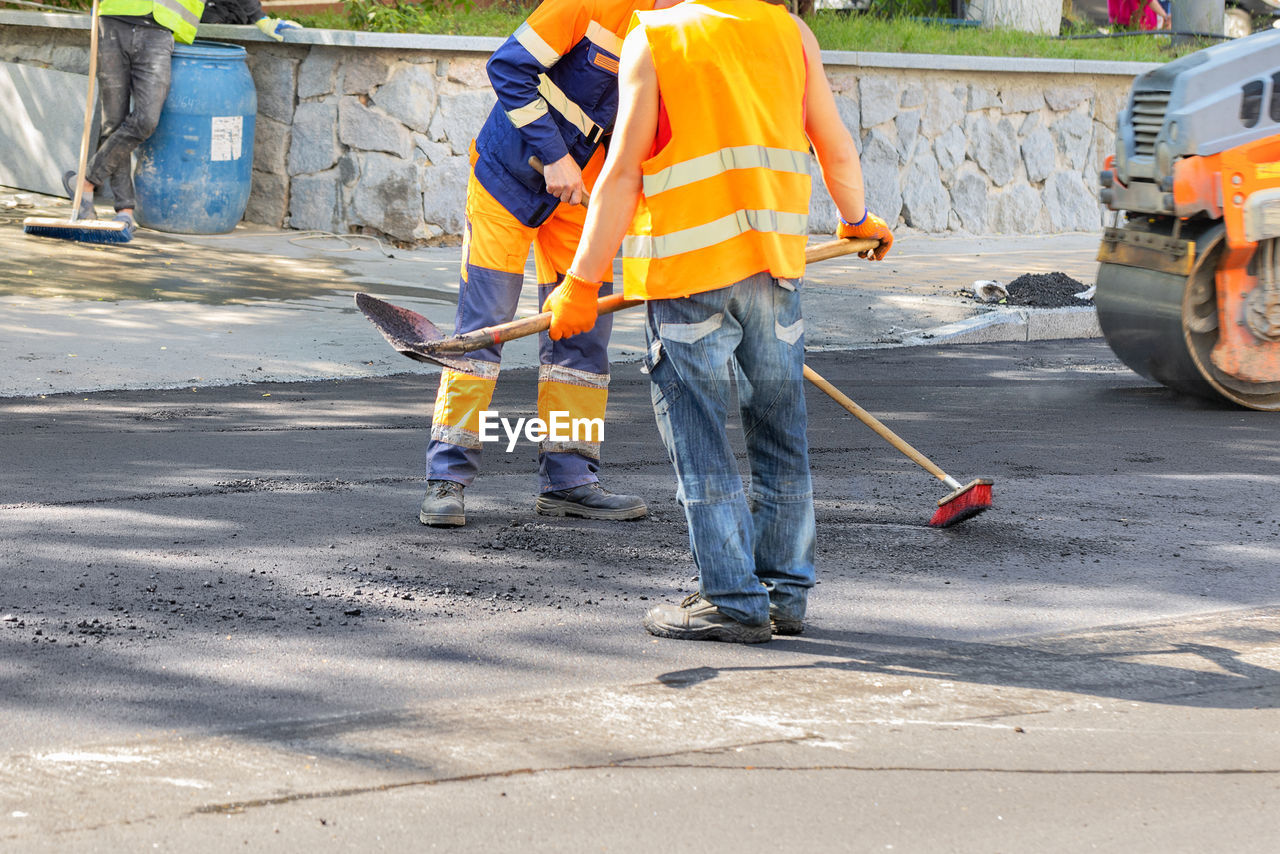 Road workers clean the asphalt pavement on the roadway with a brush and shovel.