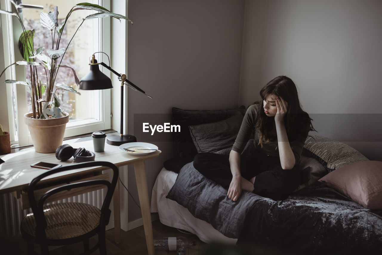 Depressed woman sitting on bed at home