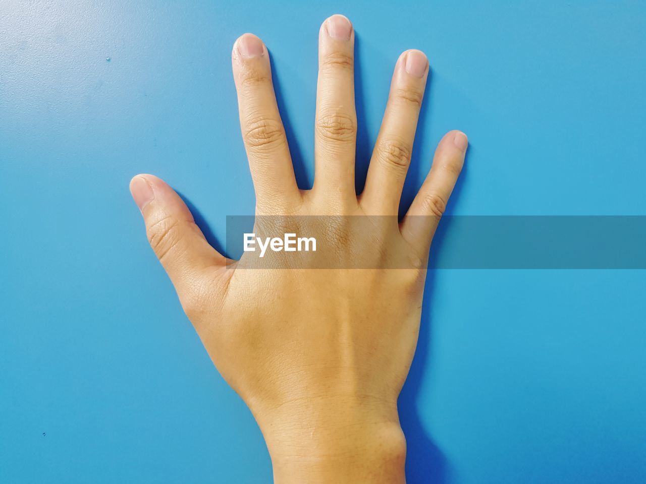 CLOSE-UP OF HUMAN HAND OVER BLUE BACKGROUND