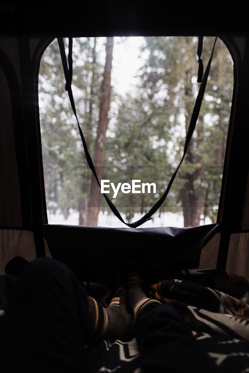 Pov shot of anonymous traveler resting inside camping vehicle parked in snowy winter forest with coniferous trees