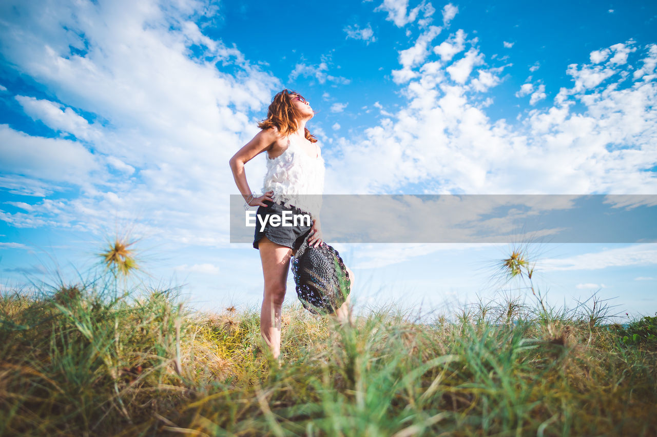 Full length of young woman standing on field against sky