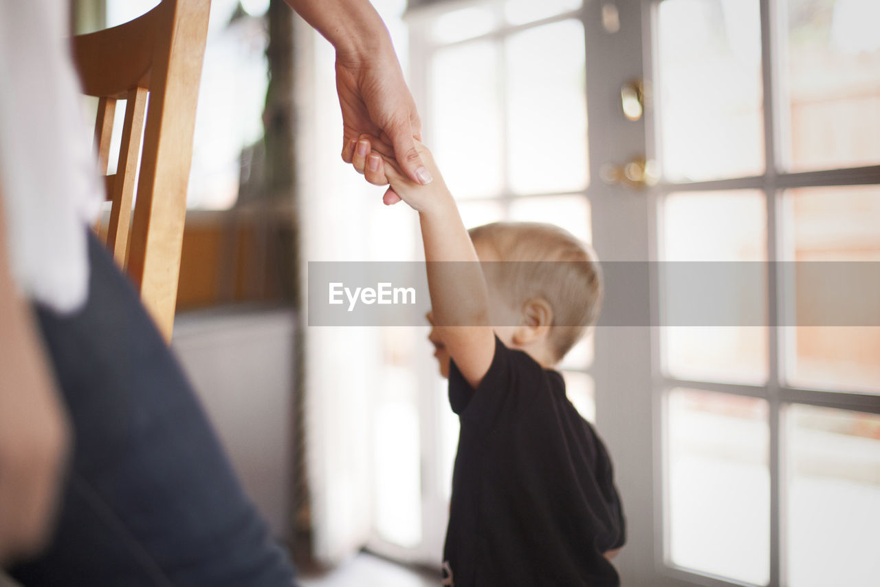 Cropped image of mother holding son's hand at home