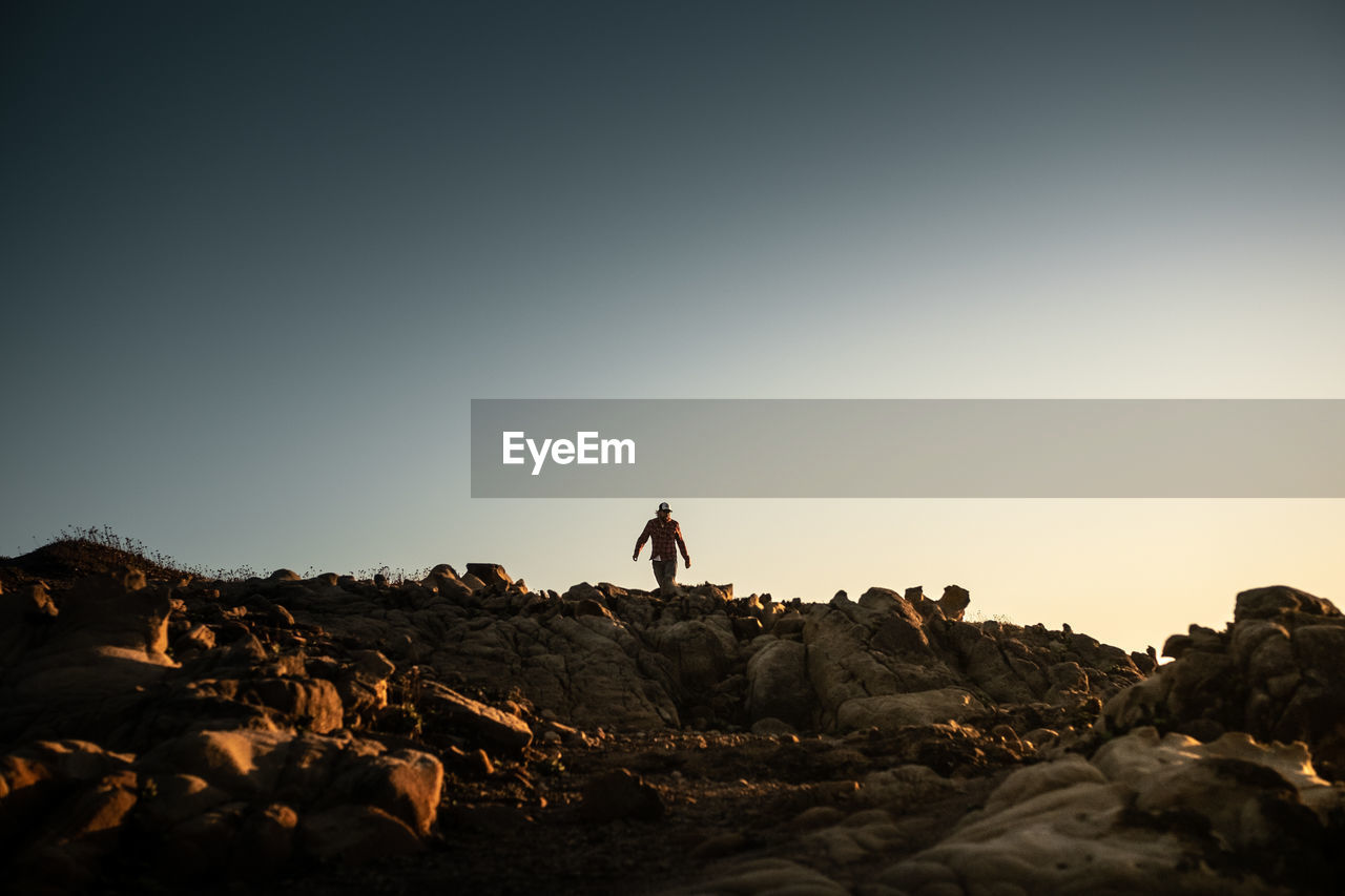 Man standing on rock against sky