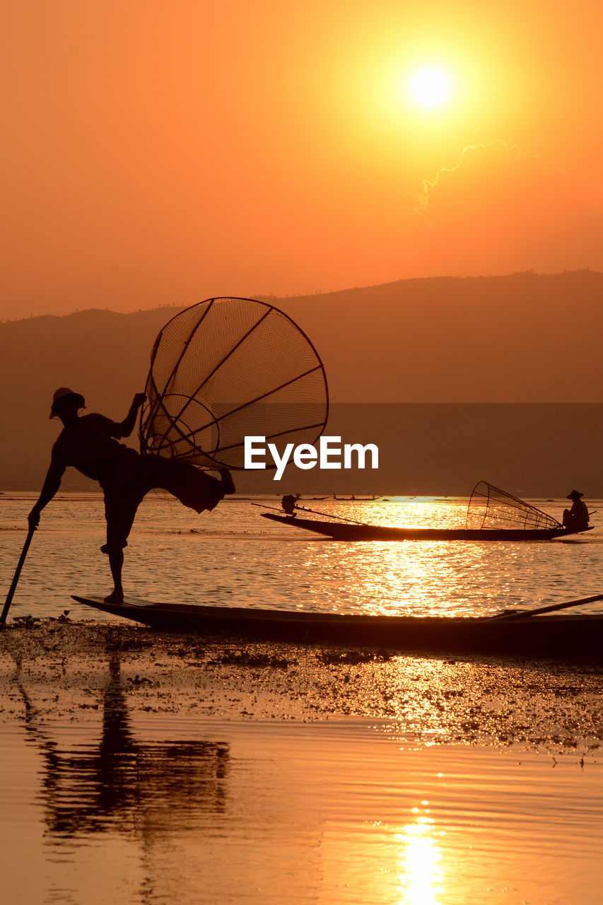 Silhouette men fishing in lake during sunset