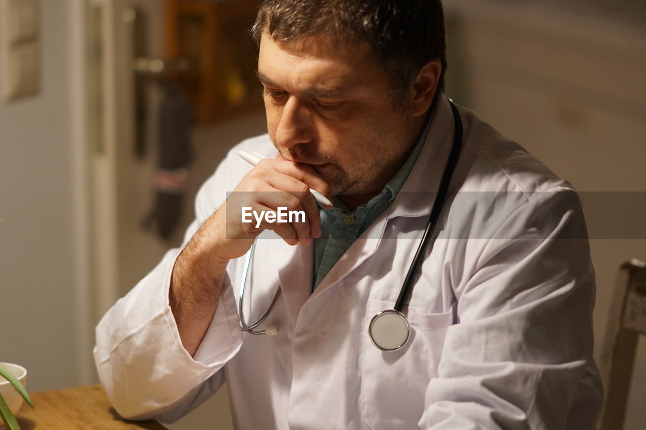 Thoughtful mature doctor with pen working in hospital