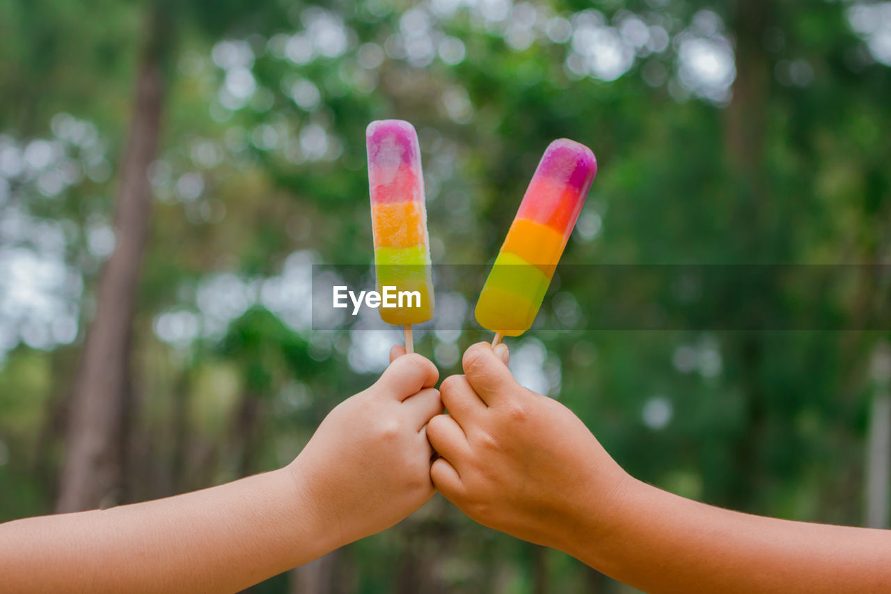 Cropped hands of people holding popsicles against trees