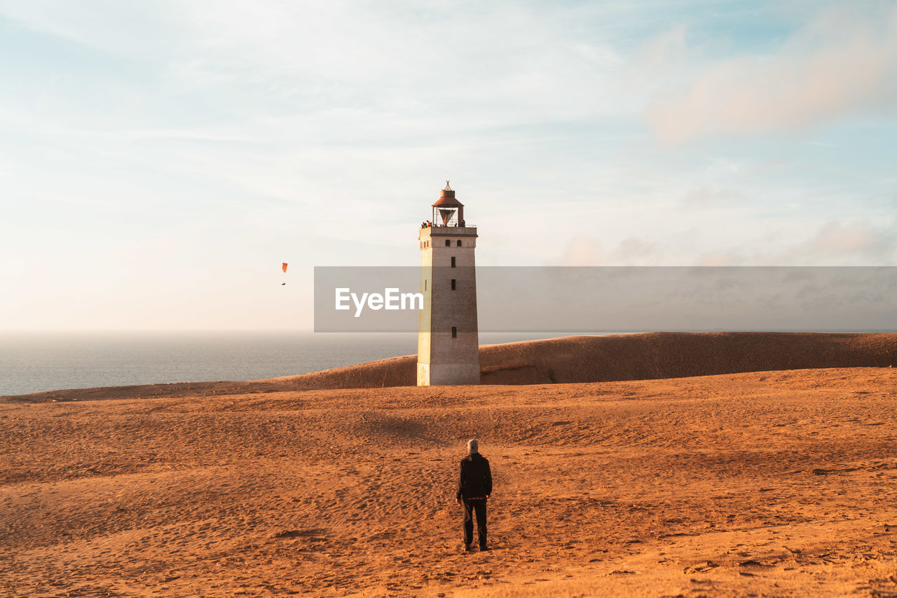 Man walking towards lighthouse by sea against sky