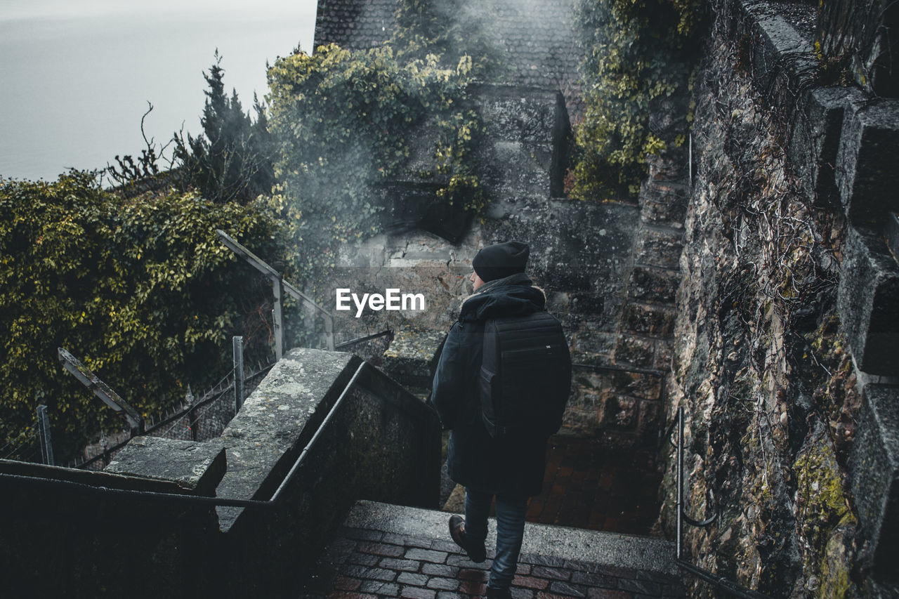 REAR VIEW OF MAN WALKING BY BUILDING AGAINST TREES