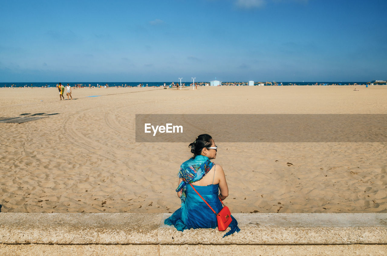 FULL LENGTH OF WOMAN SITTING ON BEACH AGAINST SEA