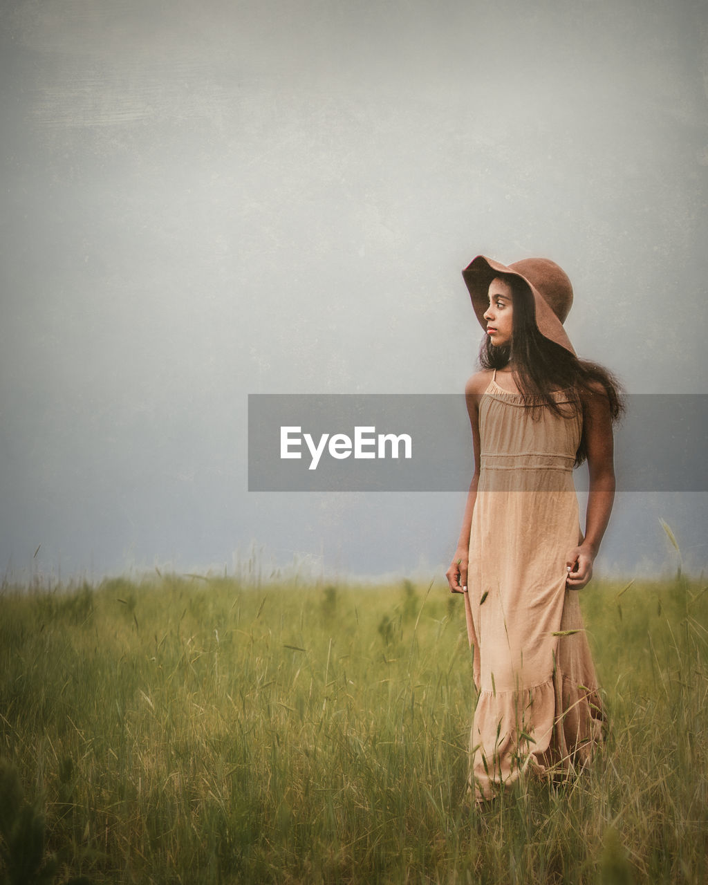 Thoughtful girl standing on grassy land against clear sky