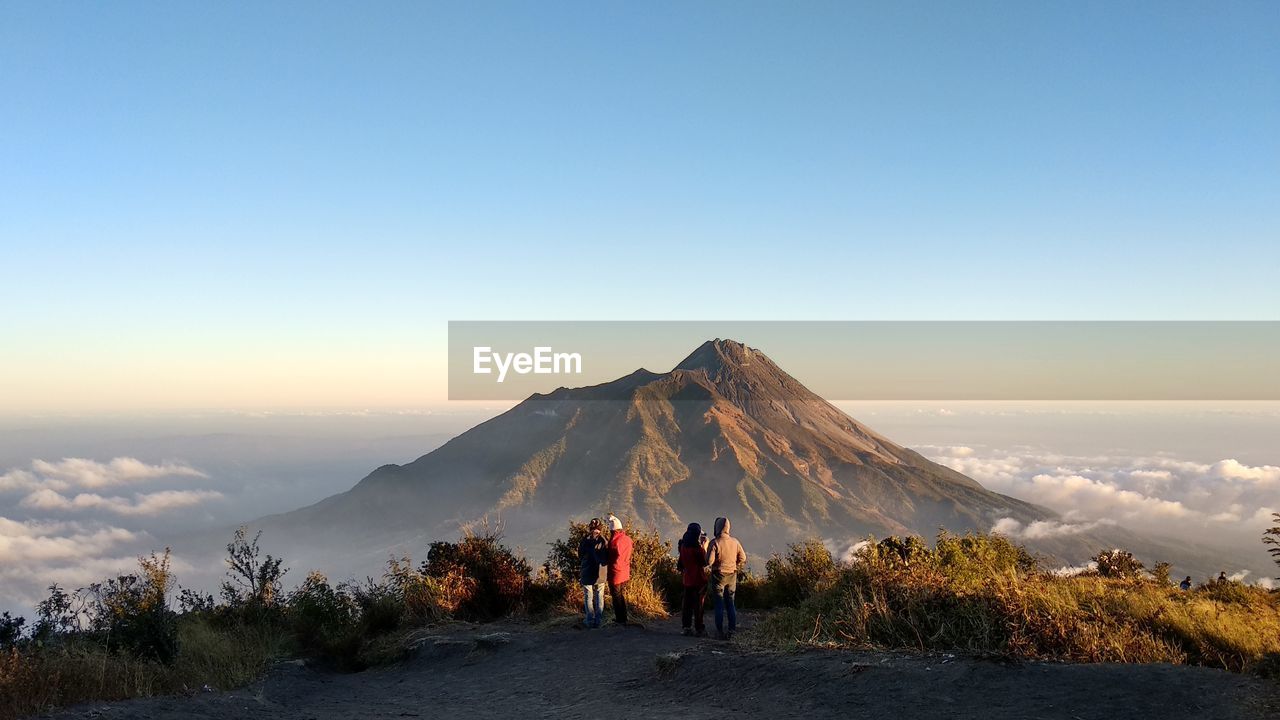 Rear view of people looking at mountain against clear sky