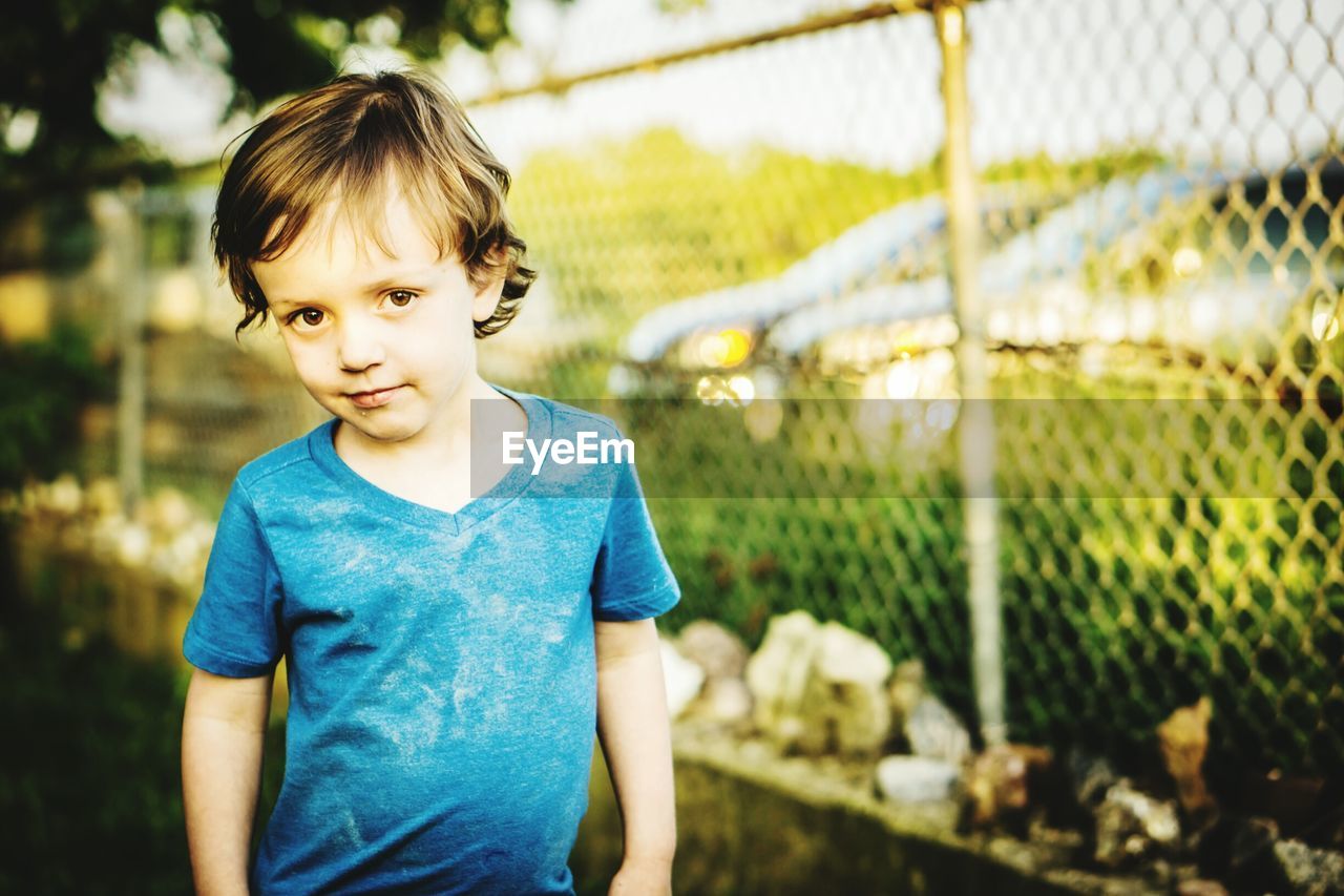 Portrait of cute boy standing against fence