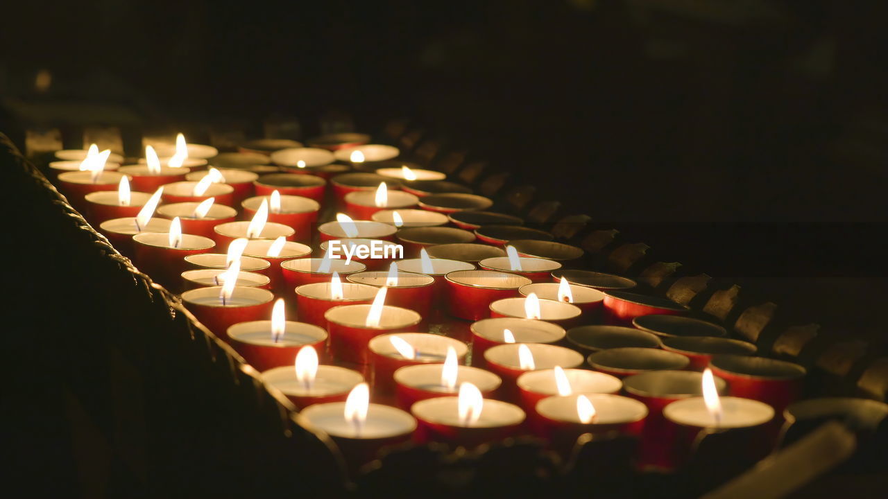 CLOSE-UP OF LIT CANDLES IN ILLUMINATED TEMPLE