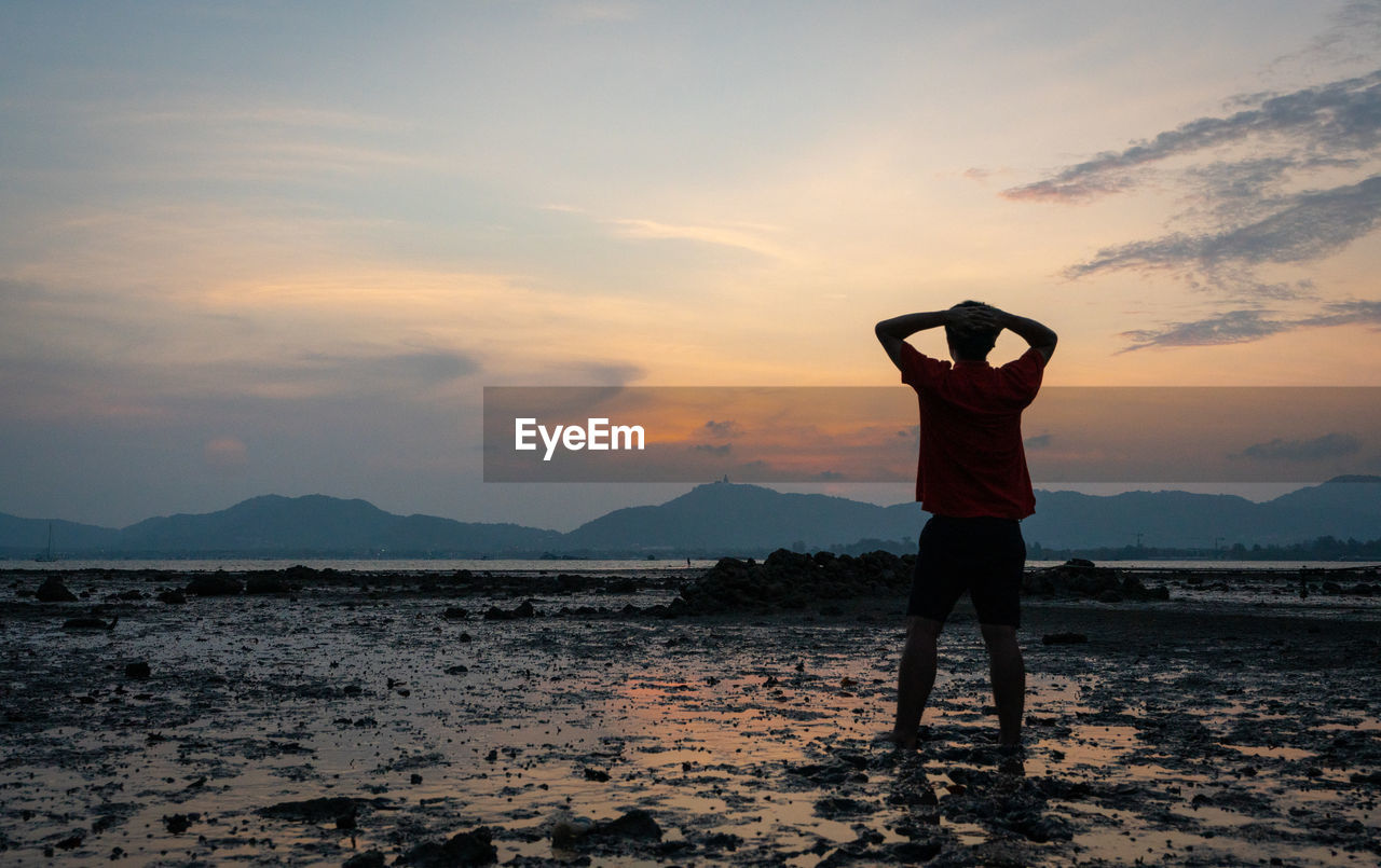 REAR VIEW OF PERSON STANDING ON LAND DURING SUNSET