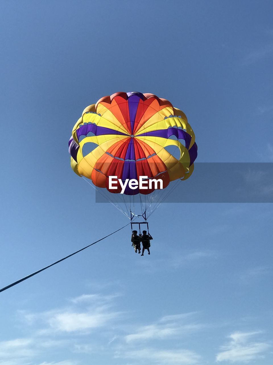 Low angle view of people parasailing against sky