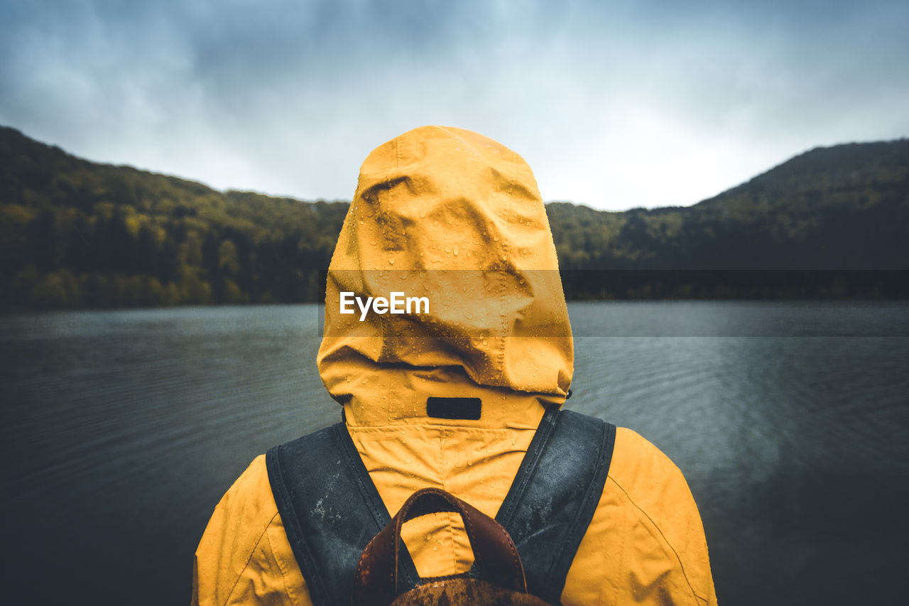 Man in hood looking at lake against sky