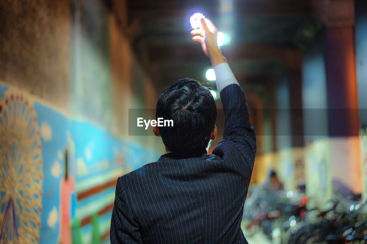 Rear view of man holding illuminated lighting equipment in city at night