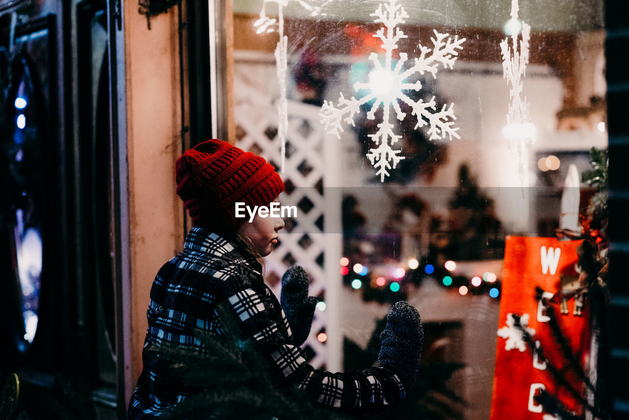 Girl looking at christmas decorations through glass at night