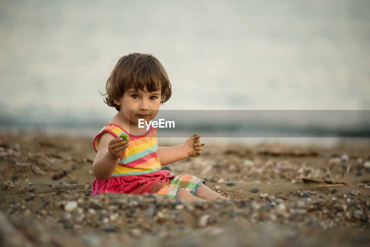 Adorable toddler baby playing on a beach with pebble stones.