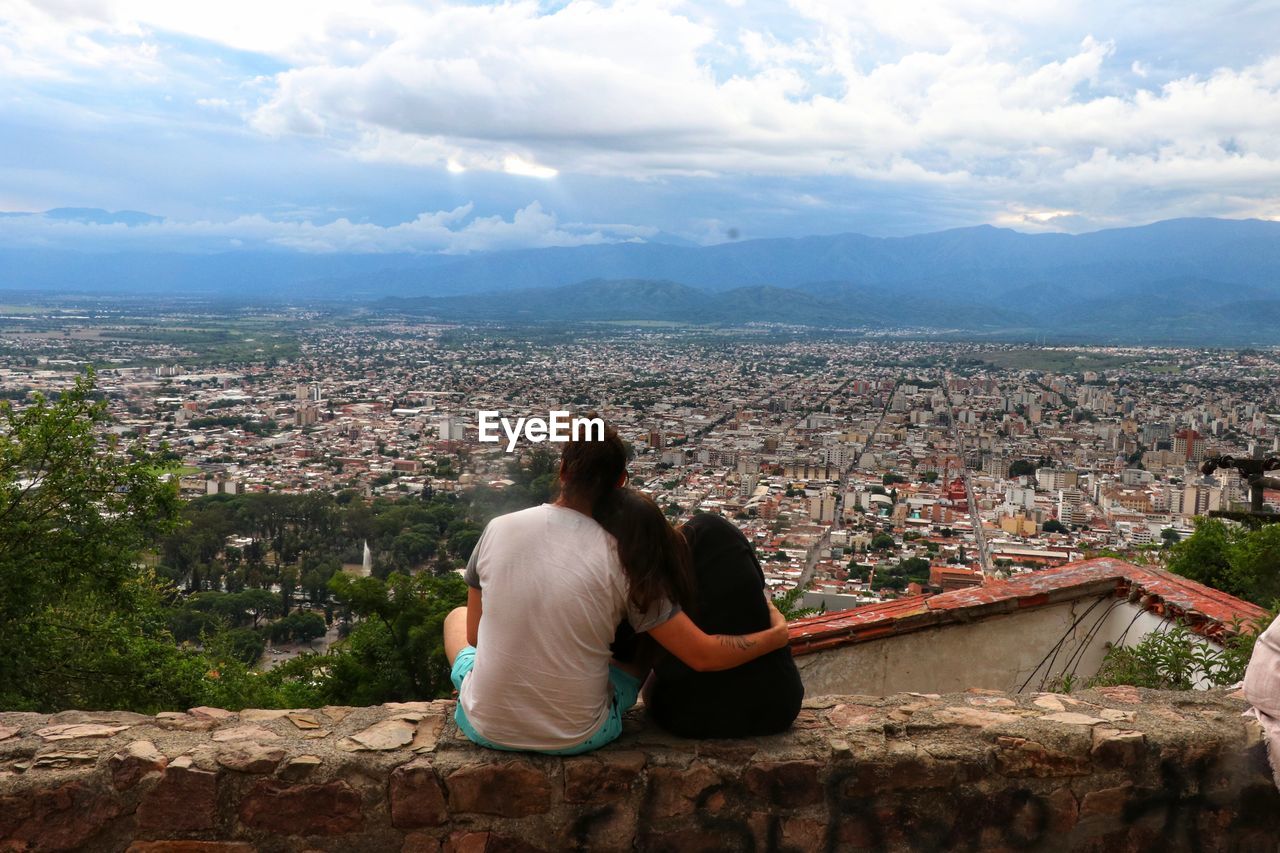 REAR VIEW OF WOMAN LOOKING AT CITY AGAINST SKY