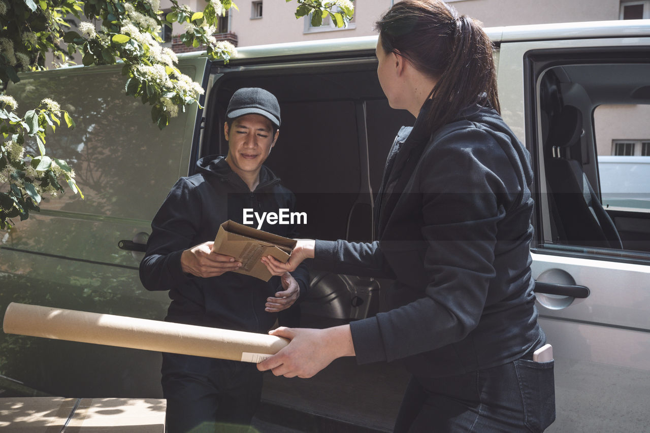 Side view of delivery woman giving package to colleague outside truck