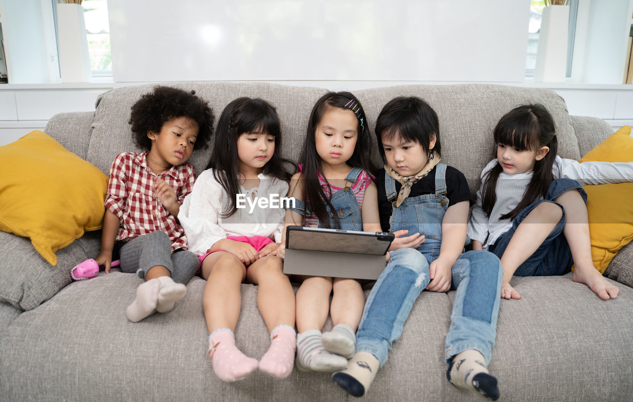 High angle view of friends sitting with digital tablet on sofa