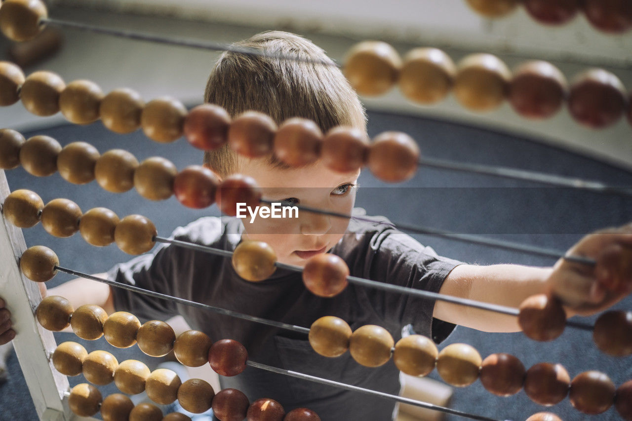 High angle view of boy leaning to count using abacus in classroom