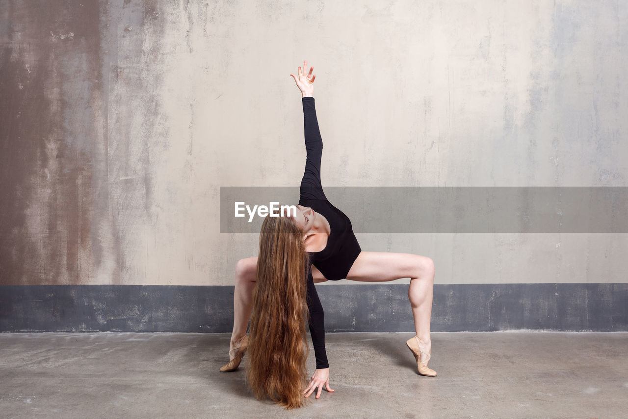 Full length of woman with arms raised while standing against wall