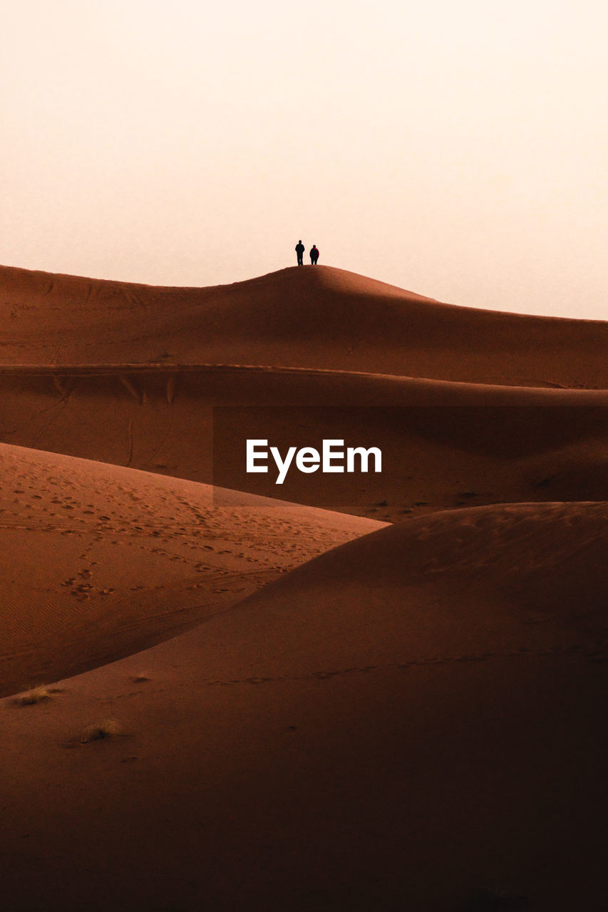 Silhouette people on sand dunes in the sahara of morocco at sunrise with golden hour lighting.  