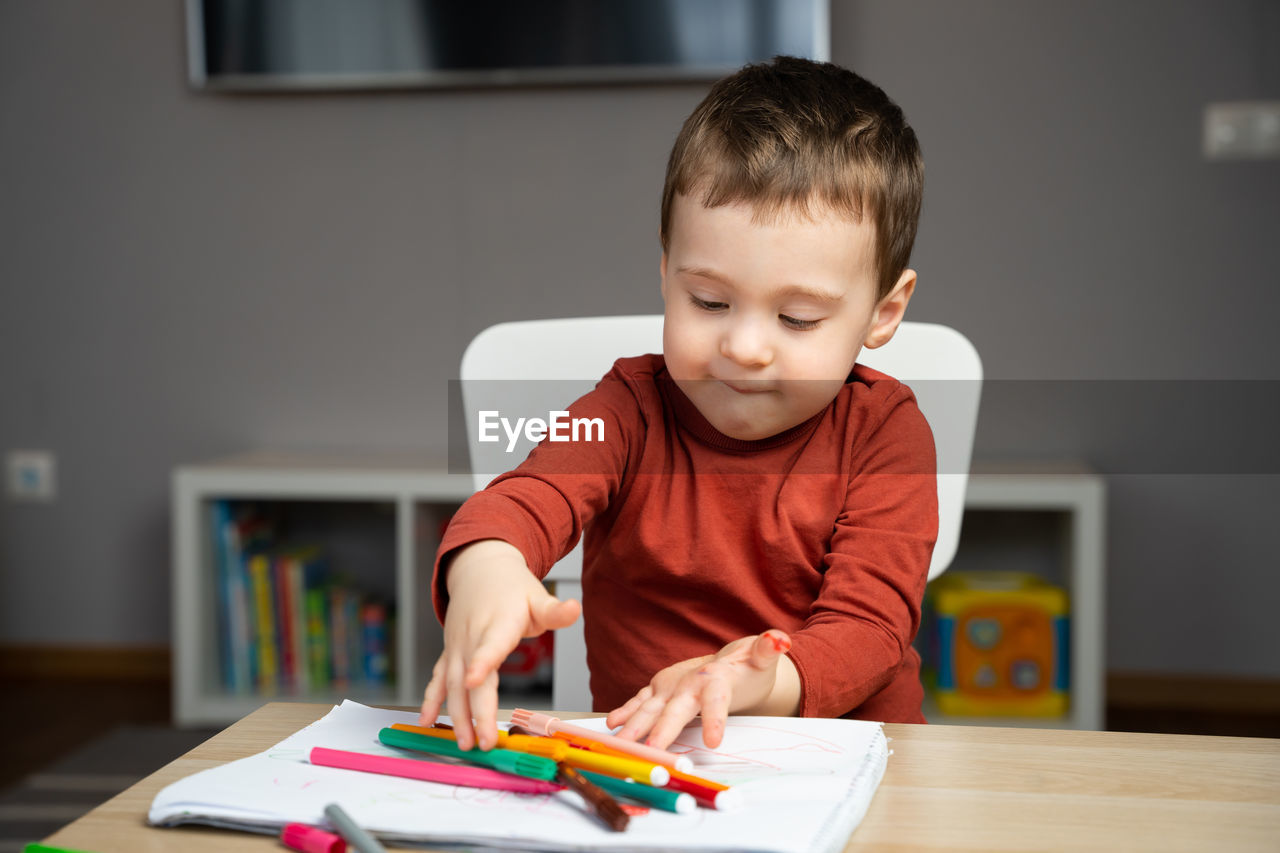 A cute happy little toddler boy of two years playing with markers in the album 