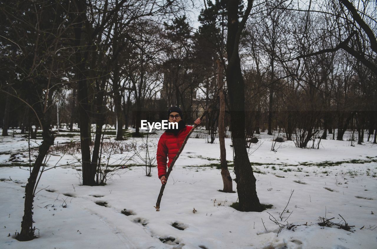 Digital composite image of man standing behind stick on snow covered field at forest