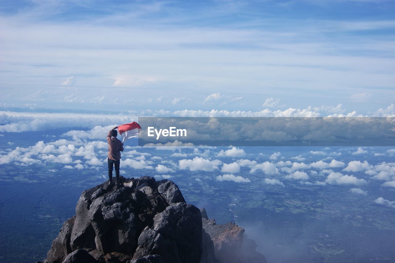 Man standing on rock by mountains against sky