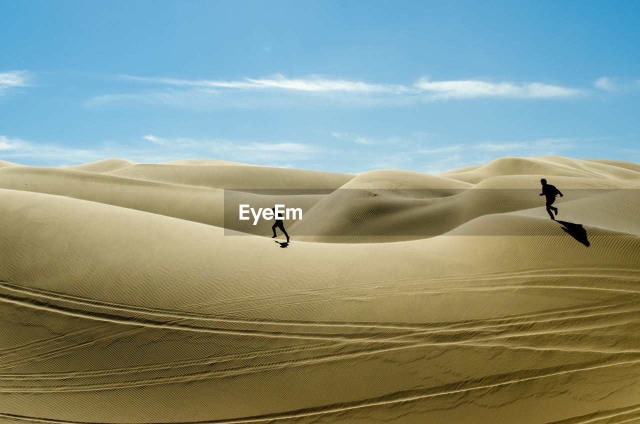 Two people running on sand dune in desert