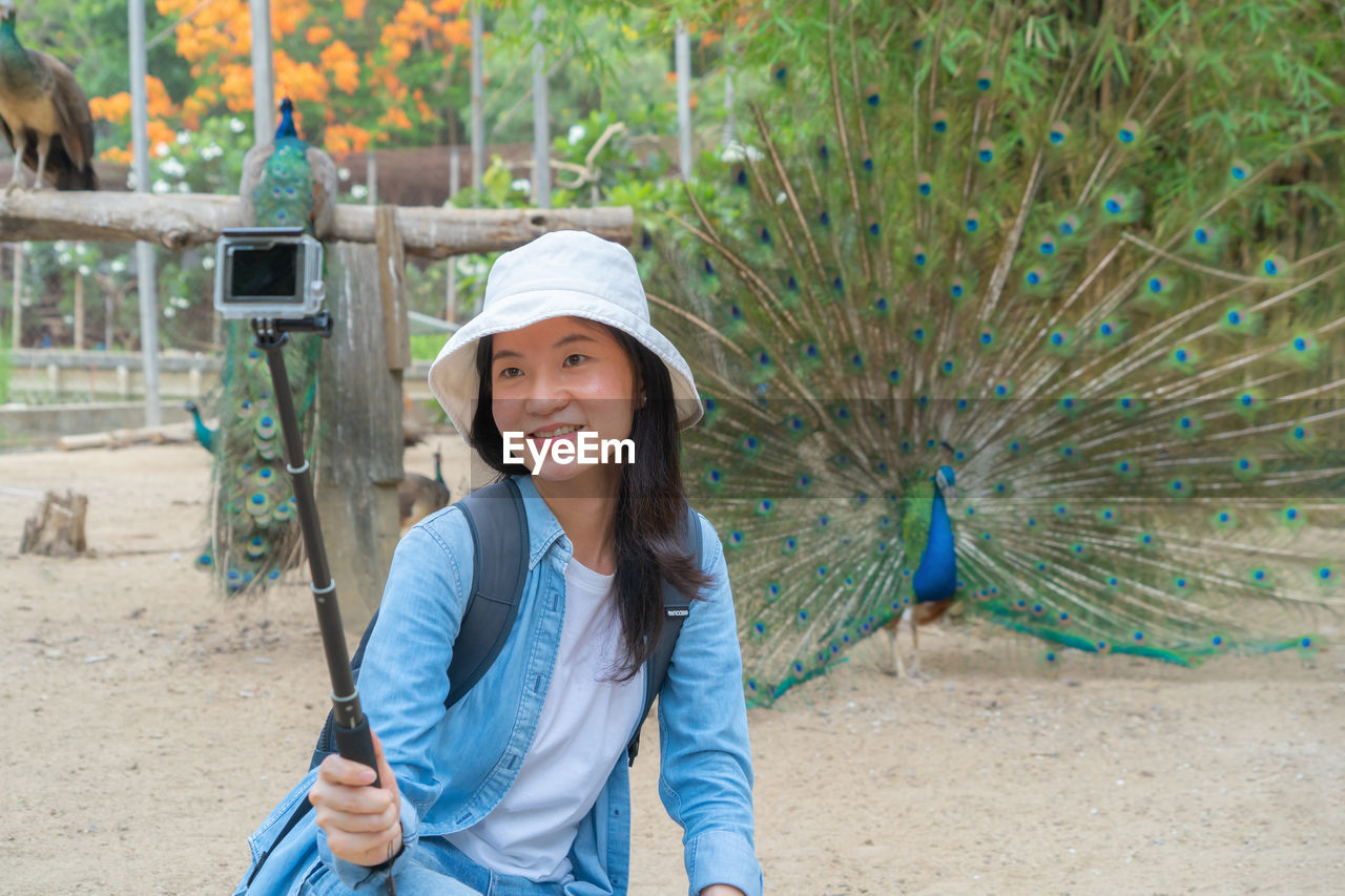 Smiling woman recording video against peacock